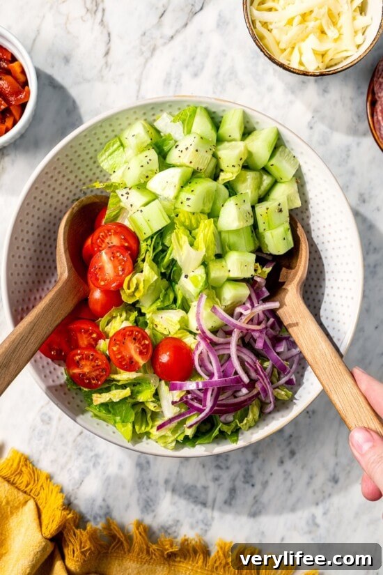Two spoons tossing Italian chopped salad in bowl.