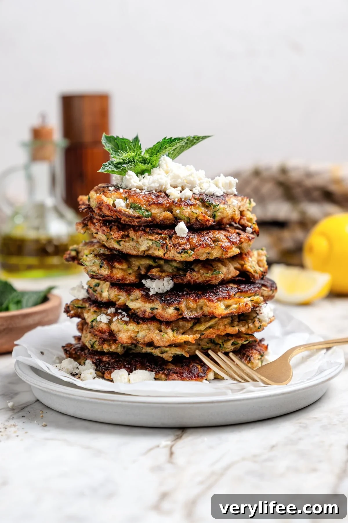 Stack of zucchini fritters on plate with feta and mint.
