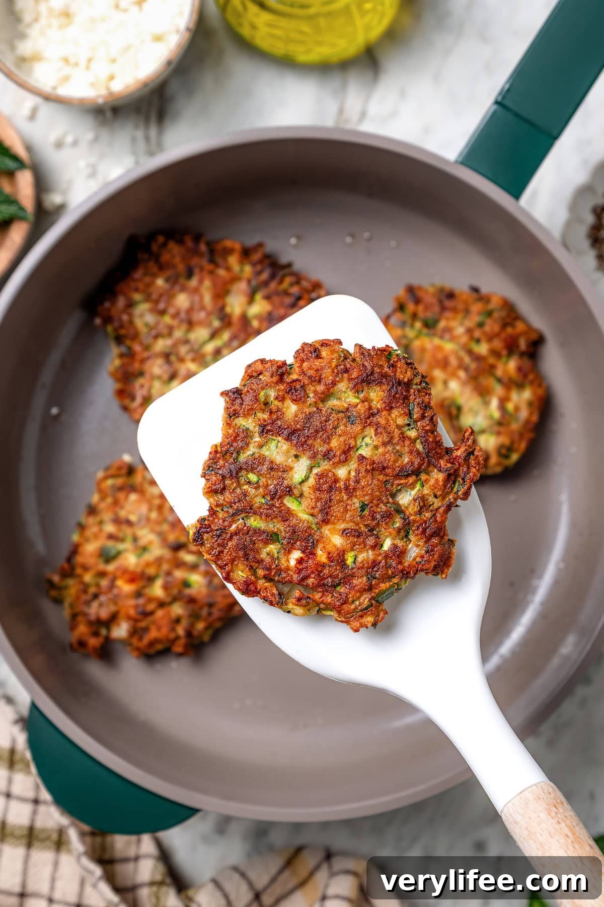 Spatula holding zucchini fritter over skillet.
