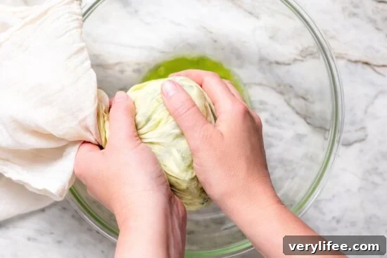 Hands squeezing zucchini wrapped in cheesecloth to remove moisture.