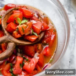 Spoon scooping tomato salad from bowl.