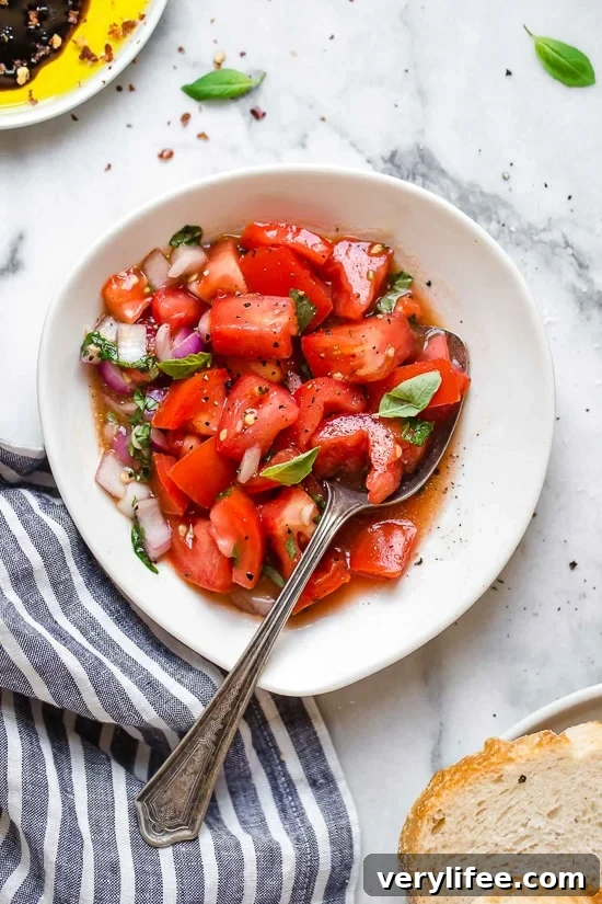 Fresh summer tomato salad with basil and seasonings. Bowl of summer tomato salad with spoon.