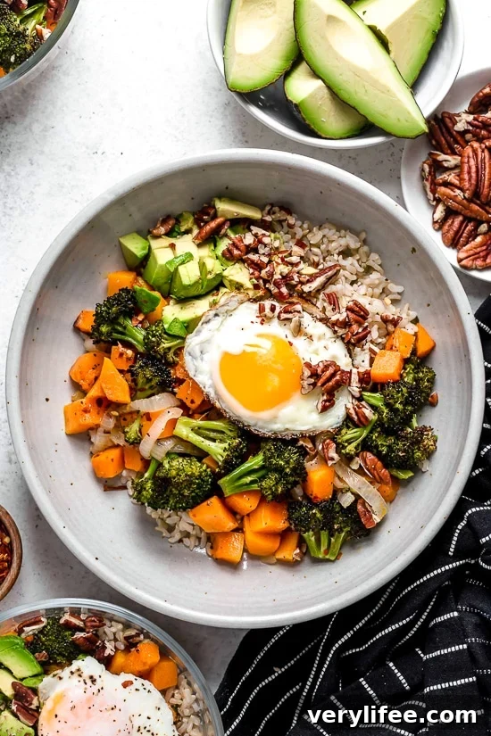This easy Buddha bowl pairs a brown rice base with roasted broccoli, butternut squash, creamy avocado, fried eggs, and pecans. So delicious! Overhead view of Buddha bowl topped with fried egg and pecans