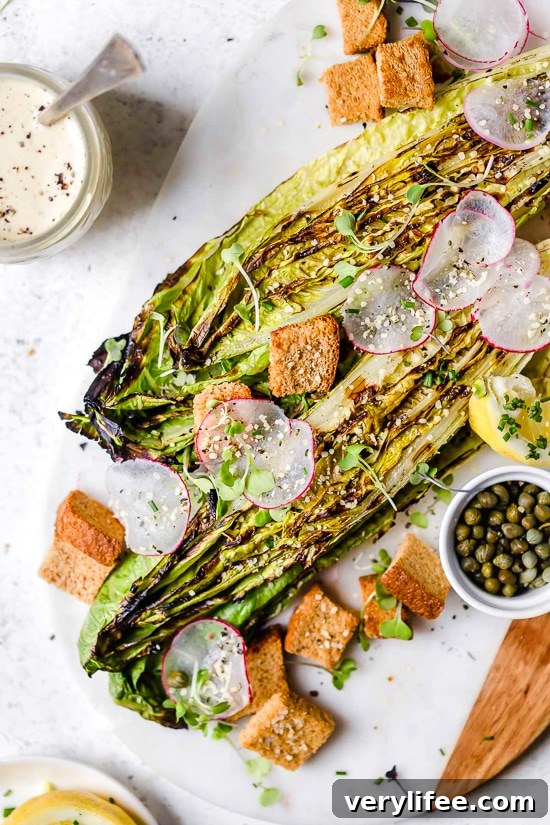 Grilled romaine salad with vegan Caesar dressing on marble and wood board.