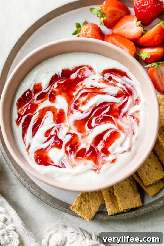 Overhead view of a bowl of strawberry cheesecake dip surrounded by mini graham crackers and fresh strawberries.