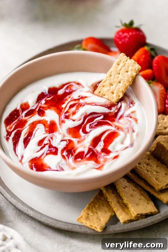 A bowl of strawberry cheesecake dip surrounded by mini graham crackers and fresh strawberries.