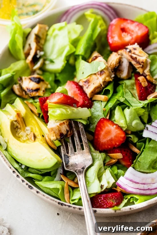 Grilled chicken salad with strawberries, avocado, toasted almonds, and citrus dressing in a bowl.
