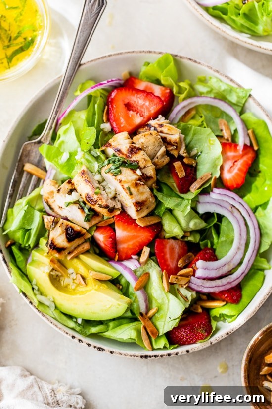 Grilled chicken salad with strawberries, avocado, toasted almonds, and citrus dressing in a bowl.