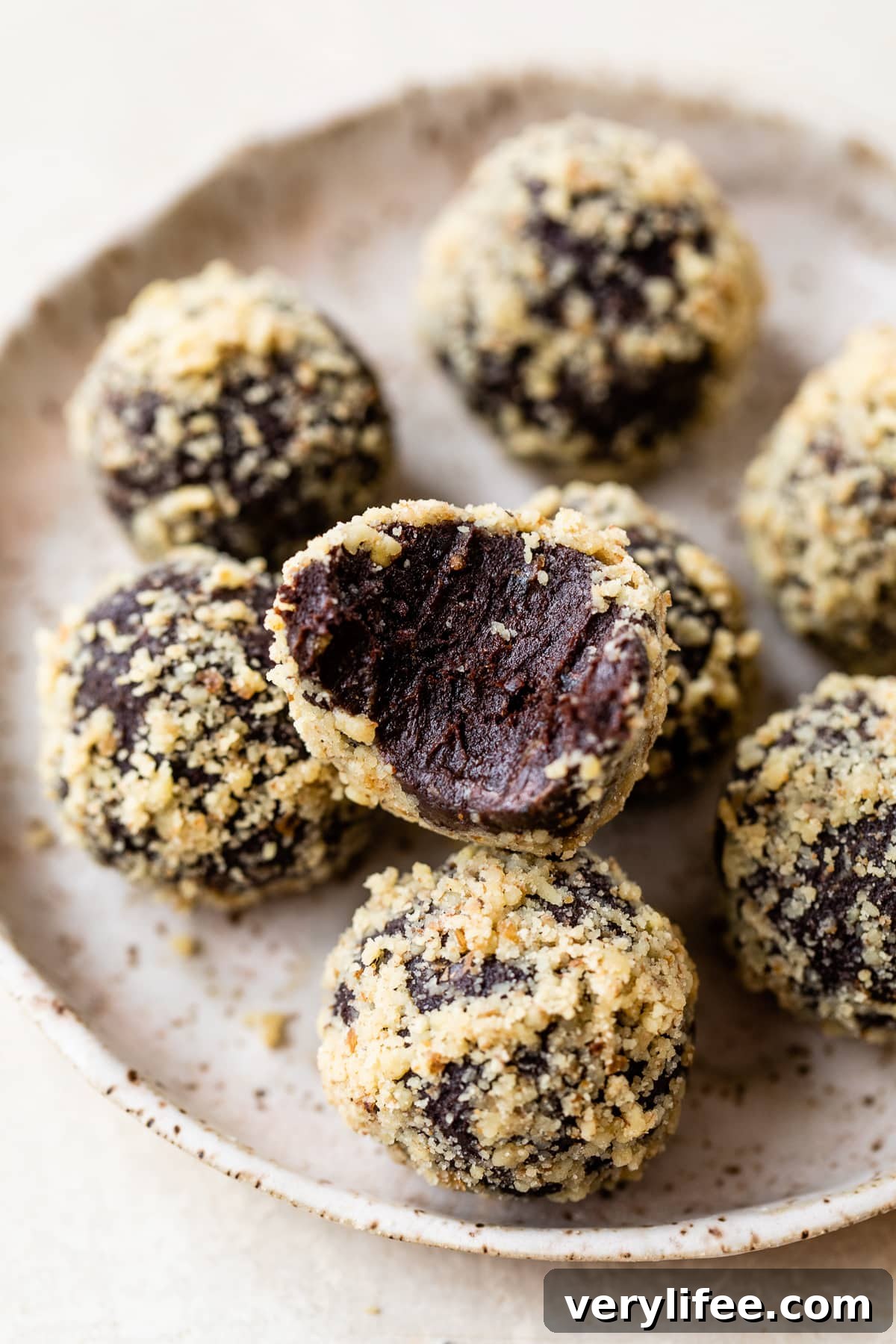 A plate of chocolate date balls, one with a bite missing to show the fudgy inside.