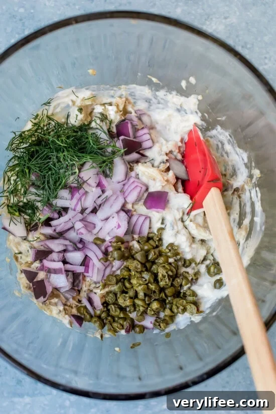 Sardine Salad Recipe with Lemon, Capers and Olive Oil 7 Mixing sardine salad with chopped onions, dill, capers, and mayonnaise in a glass bowl.